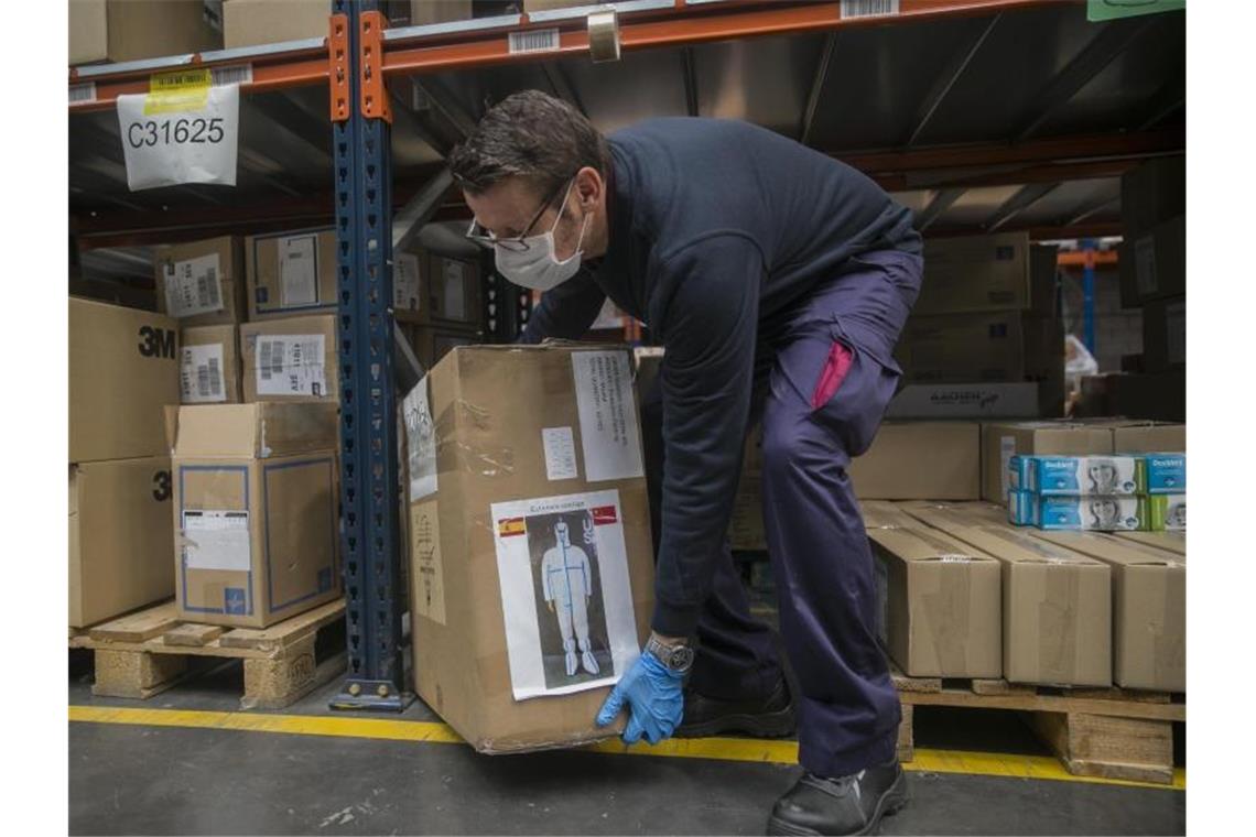 Fast 850 Corona-Tote in 24 Stunden in Spanien Ein Arbeiter trägt eine Kiste mit Schutzanzügen im Hafen von Sevilla. Foto: María José López/Europa Press/dpa