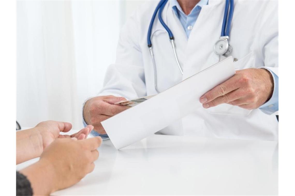 Ein Arzt hält ein Blatt Papier in der Hand. Foto: Christin Klose/dpa-tmn