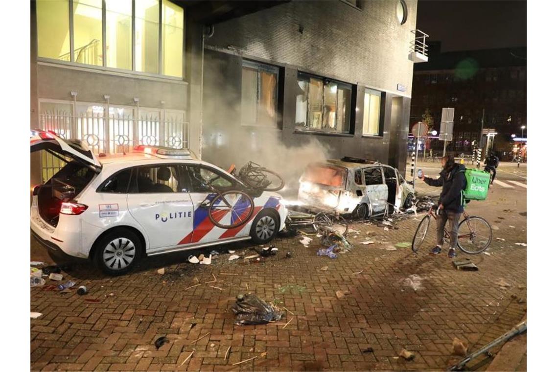 Ein ausgebranntes Auto, daneben ein beschädigter Polizeiwagen. Foto: -/ANP/dpa