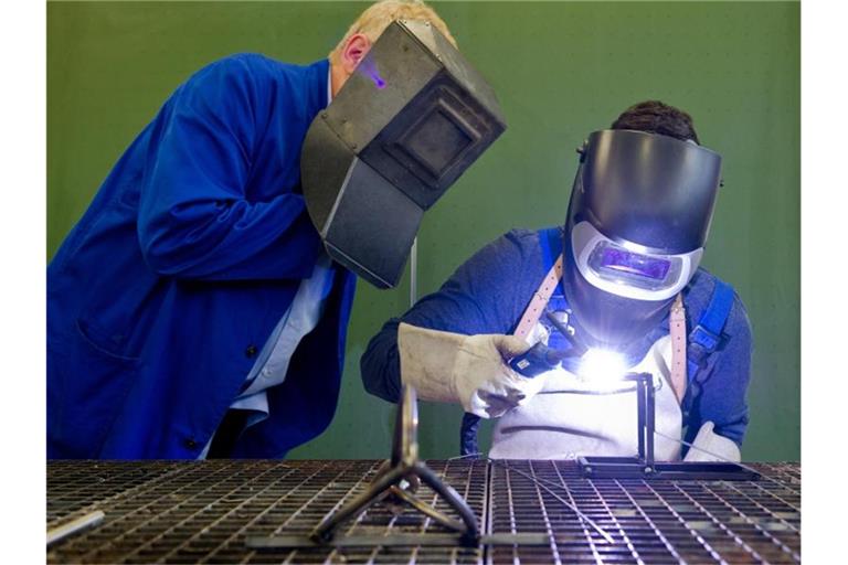 Ein Auszubildender (r) setzt eine Schweißnaht an ein Metallteil. Foto: Daniel Bockwoldt/dpa