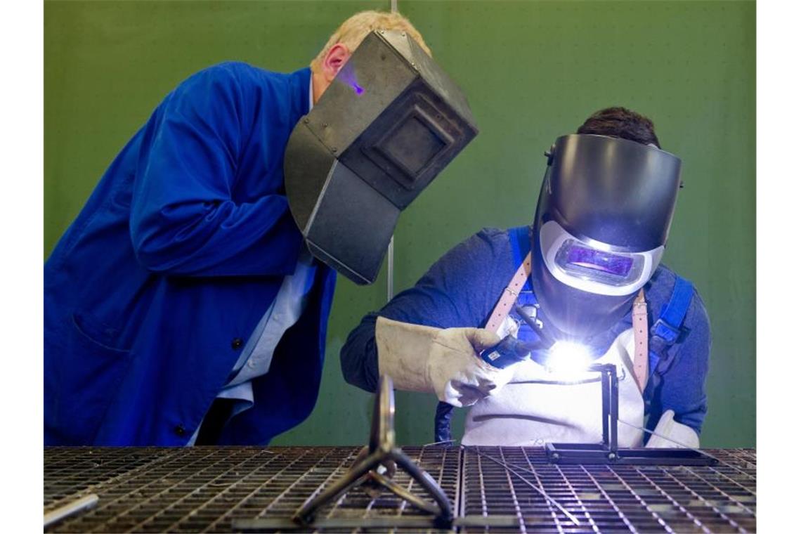 Merkel macht Druck für Digitalisierung der Ausbildung Ein Auszubildender setzt eine Schweißnaht an ein Metallteil, während ein Berufsschullehrer zuschaut. Laut Bildungsministerin Karliczek sollen „in nächster Zeit vor allem die Lehrkräfte in den Berufsschulen“ weitergebildet und „auch die Ausstattung der Berufsschulen“ verbessert werden. Foto: picture alliance / dpa