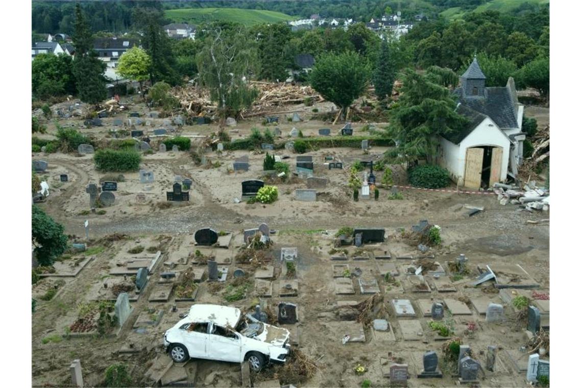 Hätte der Kreis Ahrweiler früher warnen können? Ein Auto, das bei der Hochwasserkatastrophe auf den Friedhof geschwemmt worden ist, steht auf einem Grabfeld. Der Friedhof ist völlig zerstört. Foto: Thomas Frey/dpa