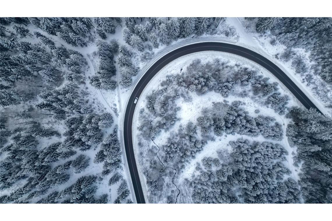 Ein Auto fährt auf einer Landstraße durch den winterlichen Wald im Vogtland.