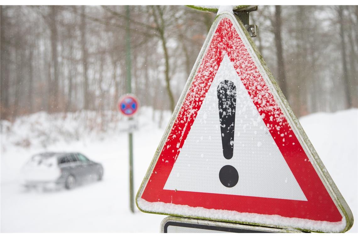 Ein Auto fährt über eine zugeschneite Straße beim nordrhien-westfälischen Bielefeld, daneben ist ein Verkehrsschild mit einem Gefahrenzeichen zu sehen.