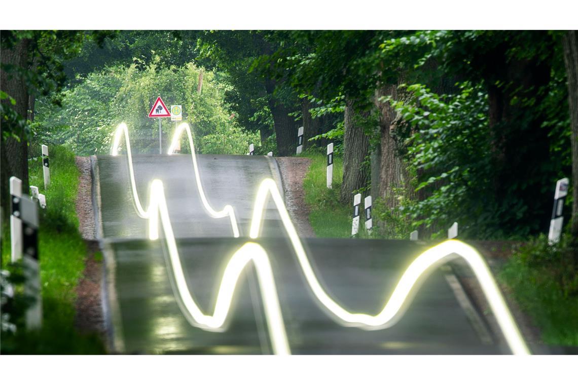 Bilder des Tages Ein Auto hinterlässt wellige Lichtstreifen, die durch eine Aufnahme mit langer Belichtungszeit entstehen, als es mit Licht am frühen Morgen durch eine Allee fährt.