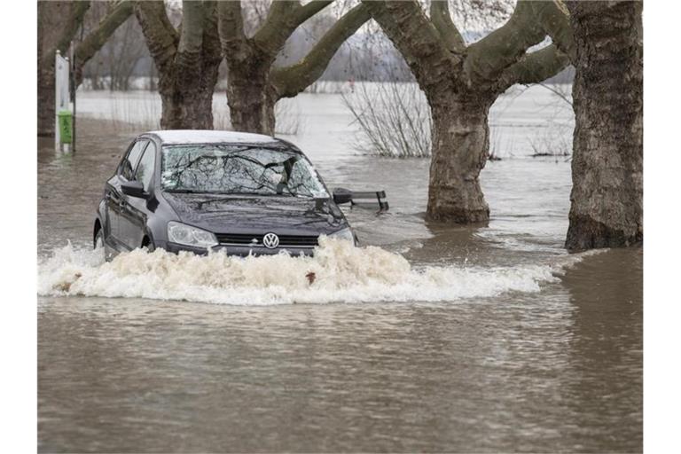 Ein Autofahrer steuert in Rüdesheim am Rhein seinen Wagen über eine vom Hochwasser überflutete Straße. Foto: Boris Roessler/dpa