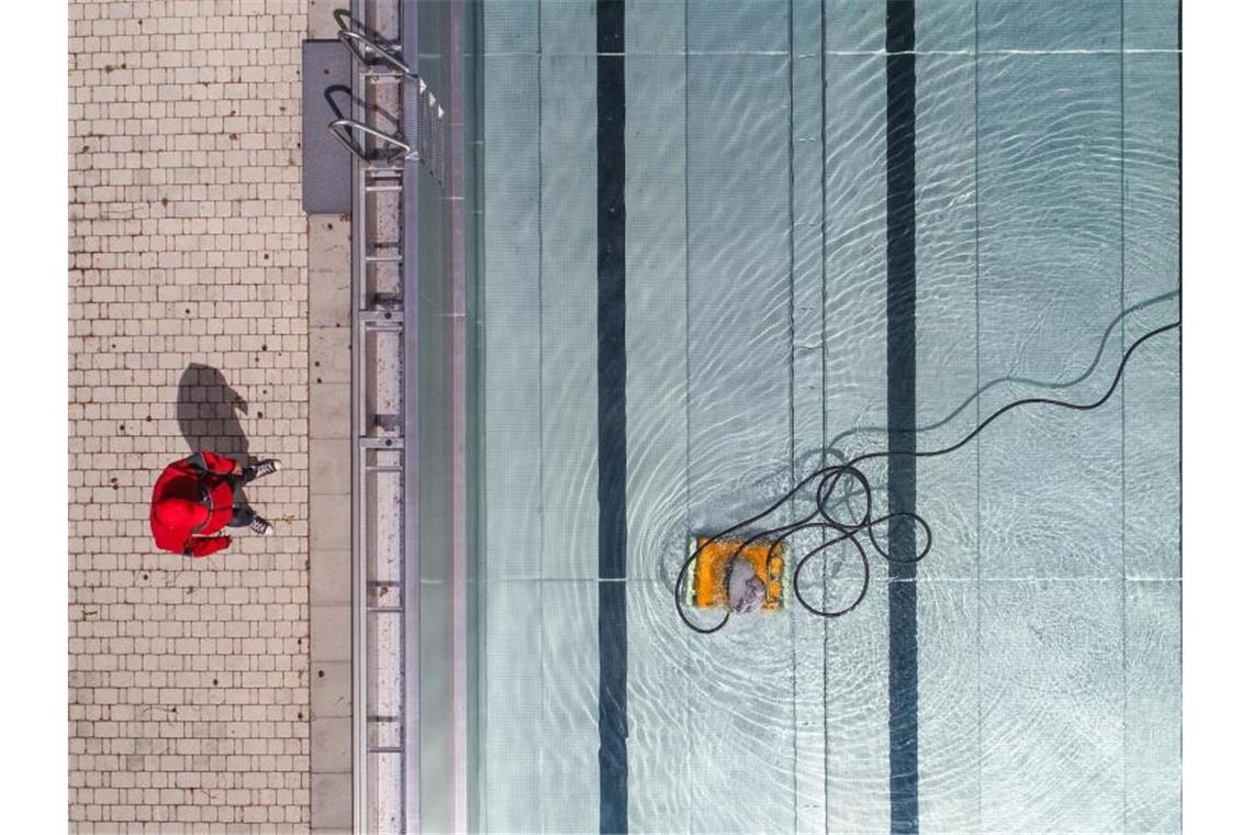 Ein Badleiter steht in einem Freibad am Beckenrand, und prüft die Arbeit eines Pool-Reinigungsroboters. Foto: Patrick Pleul/dpa-Zentralbild/dpa