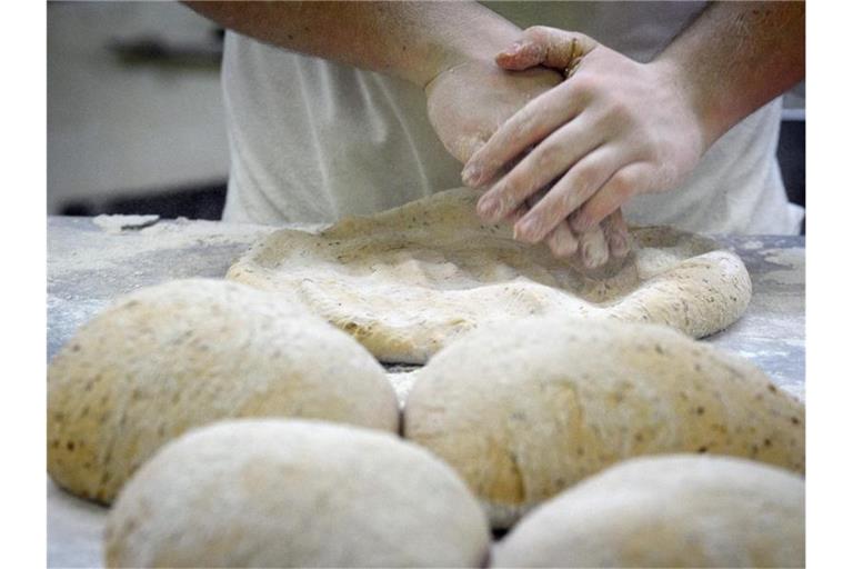 Ein Bäcker formt in der Backstube auf einer Arbeitsplatte Teig. Foto: Soeren Stache/dpa/Symbolbild