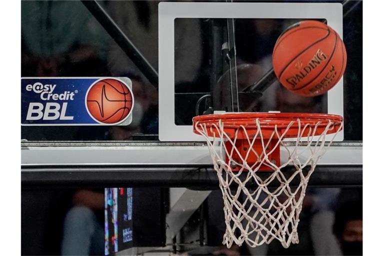 Ein Ball fliegt auf den Korb zu, an dem ein Logo der Basketball-Bundesliga klebt. Foto: Axel Heimken/dpa/Symbolbild