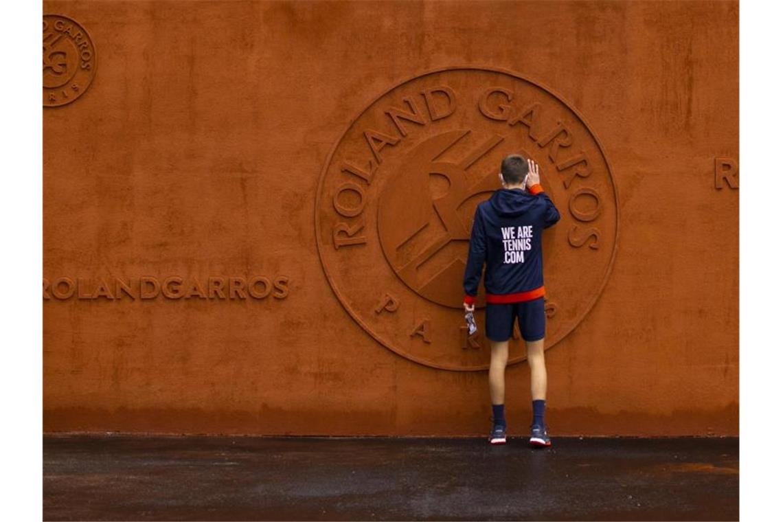 Ein Balljunge berührt das Logo vom Stade Roland Garros. Foto: Peter Dejong/AP/dpa