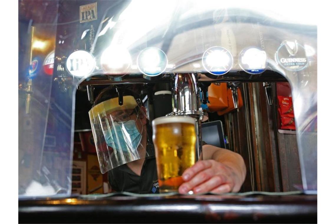 Ein Barkeeper im Pub zapft ein Glas Bier mit Mundschutz und Visier vor der Wiedereröffnung. Foto: Yui Mok/PA Wire/dpa