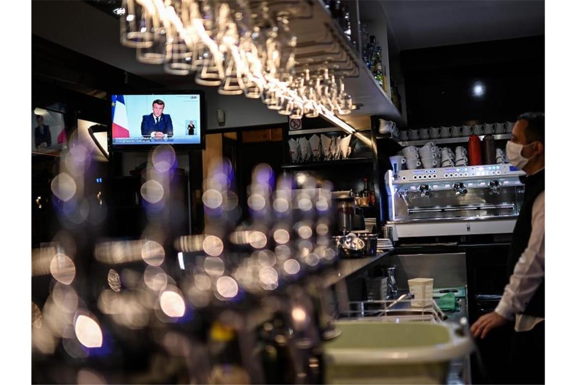 Ein Barkeeper schaut sich die Fernsehansprache von Präsident Macron in einem Café in Marseille an. Foto: Christophe Simon/AFP/dpa