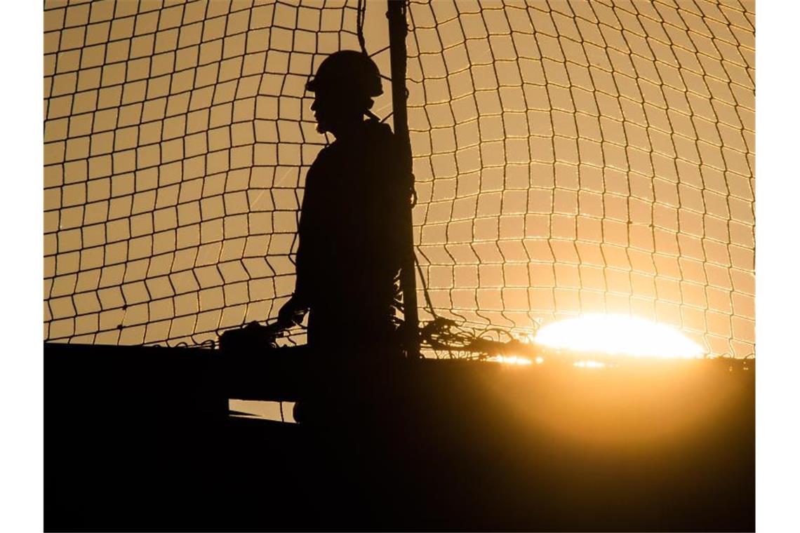 Ein Bauarbeiter bei Sonnenaufgang auf einer Baustelle auf dem Dach einer Gewerbehalle. Foto: Julian Stratenschulte/dpa