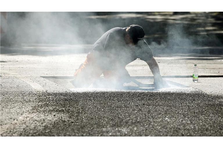 Ein Bauarbeiter repariert eine Straße in Berlin mit Bitumen, einem Bindemittel für Asphalt. (Symbolbild)
