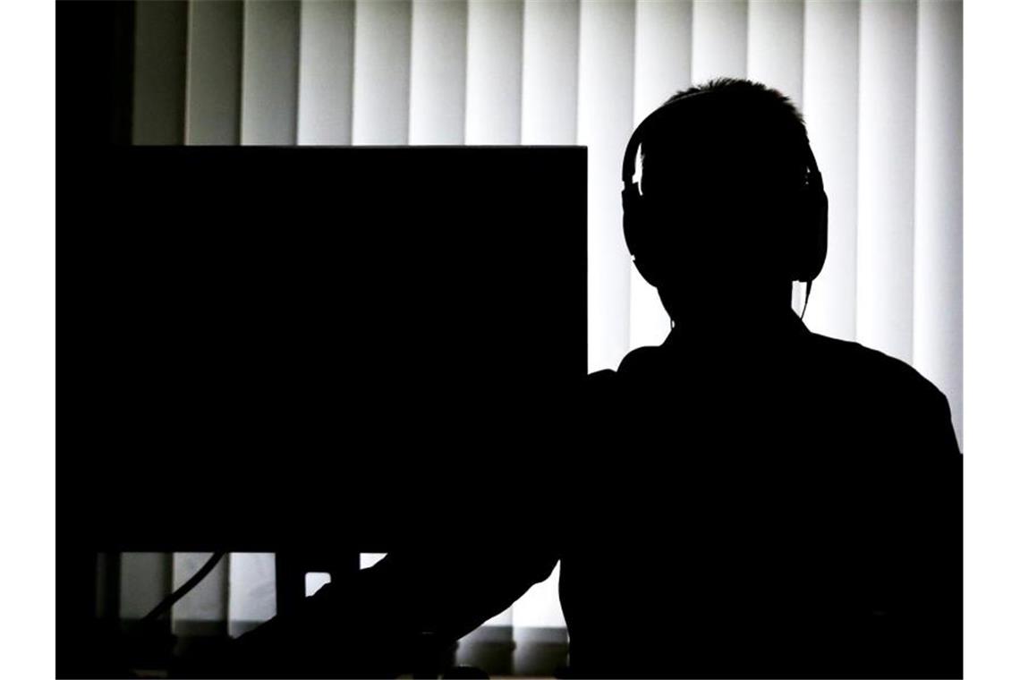 Ein Beamter sitzt für eine Telefonüberwachung mit Kopfhörern vor einem Computer. Foto: Christian Charisius/dpa/Archivbild