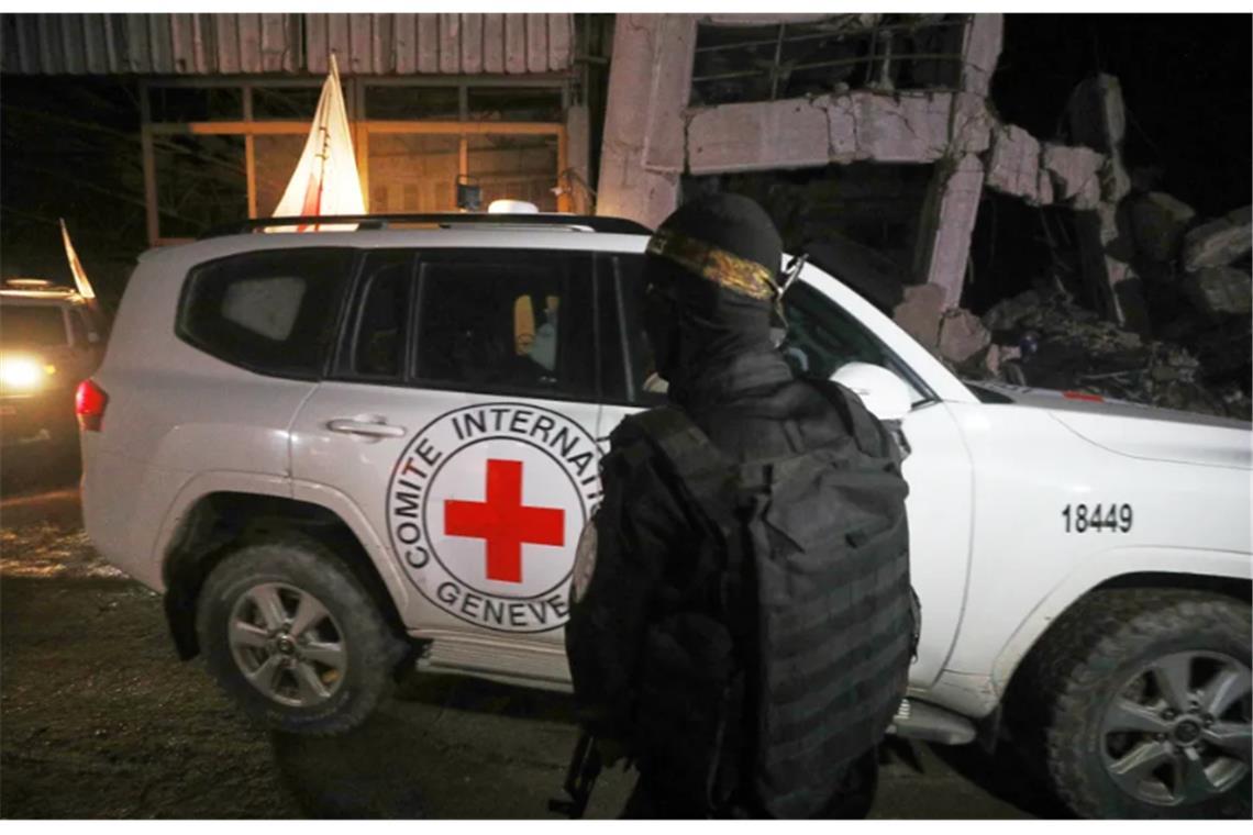 Ein bewaffneter Mann in der Uniform der al-Qassam-Brigaden, dem militärischen Flügel der Hamas, steht Wache, als Fahrzeuge des Roten Kreuzes ein Lagerhaus verlassen.