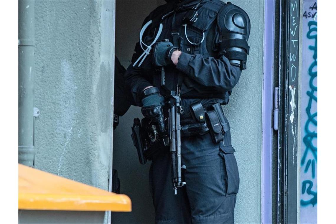 Ein bewaffneter Polizeibeamter steht an einem Wohnhaus. Foto: Paul Zinken/dpa/Symbolbild