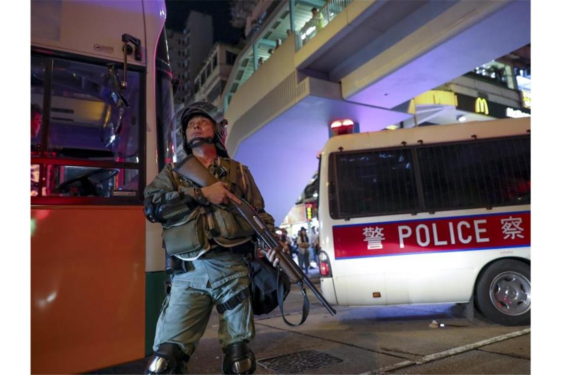 Demonstranten in Hongkong trotzen den Warnungen aus Peking Ein bewaffneter Polizist beobachtet Demonstranten, die Mülltonnen von einer Fußgängerbrücke werfen. Foto: Vincent Thian/AP