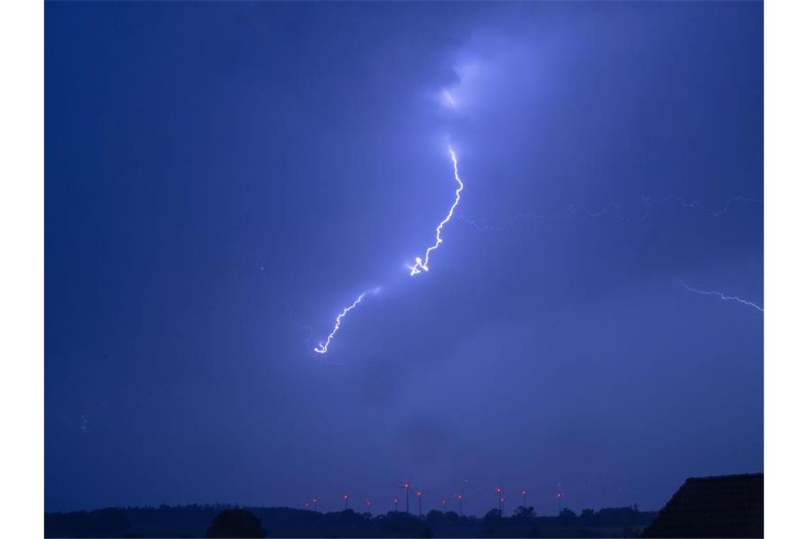 Meteorologen rechnen mit Gewitter und Hagel Ein Blitz ist bei einem starken Gewitter über einer Windkraftanlage zu sehen. Foto: Jens Büttner/Archivbild
