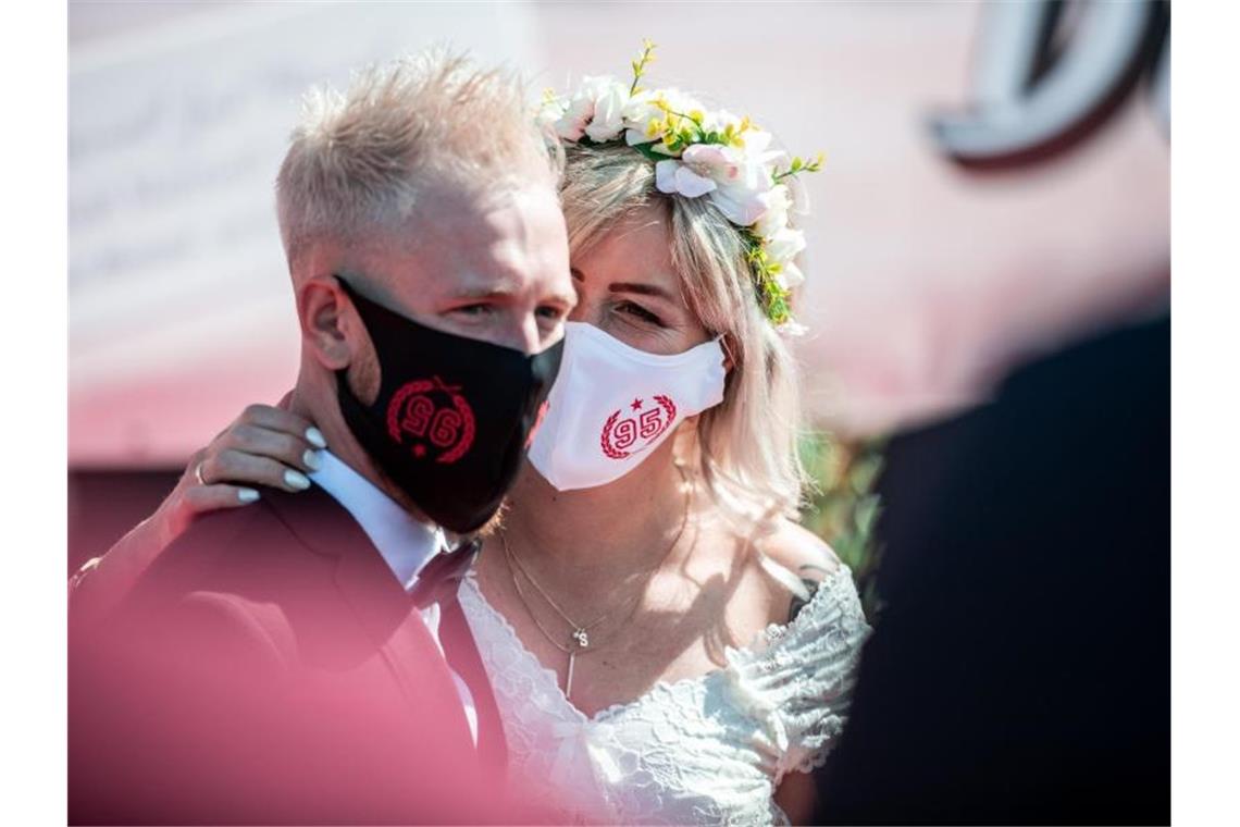 Branche befürchtet wegen Corona Engpässe in Hochzeitssaison Ein Brautpaar steht mit Mundschutz bei seiner Trauung im Autokino. Foto: Fabian Strauch/dpa/Archivbild