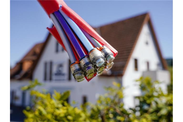 Ein Bündel mit Umhüllungen für Glasfaserkabel hängt vor einem Wohnhaus. Foto: Uwe Anspach/dpa/Archivbild