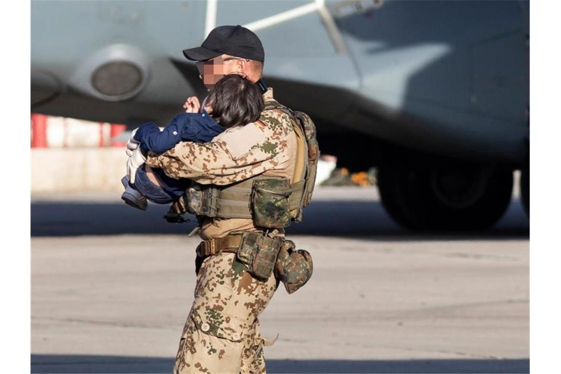 Ein Bundeswehrsoldat trägt ein Kleinkind über den Flughafen von Taschkent. Foto: Marc Tessensohn/Bundeswehr/dpa