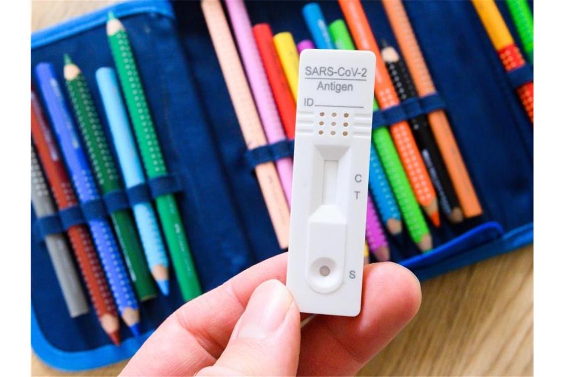 Unterricht am Limit: Omikron-Welle trifft die Schulen Ein Corona-Selbsttest wird über dem Federmäppchen eines Grundschülers gehalten. Foto: Julian Stratenschulte/dpa/Illustration