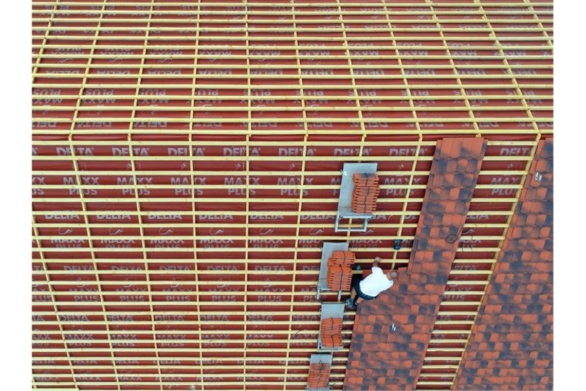 Ein Dachdecker verlegt Dachziegeln) auf einem großen Hausdach. Foto: Patrick Pleul/zb/dpa