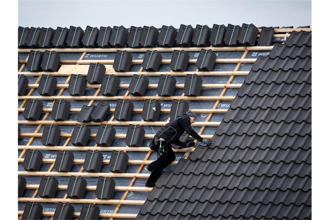 Ein Dachdeckermeister setzt eine Dachpfanne auf der Dachfläche eines Schulgebäudes. Foto: Christian Charisius/dpa/Archivbild
