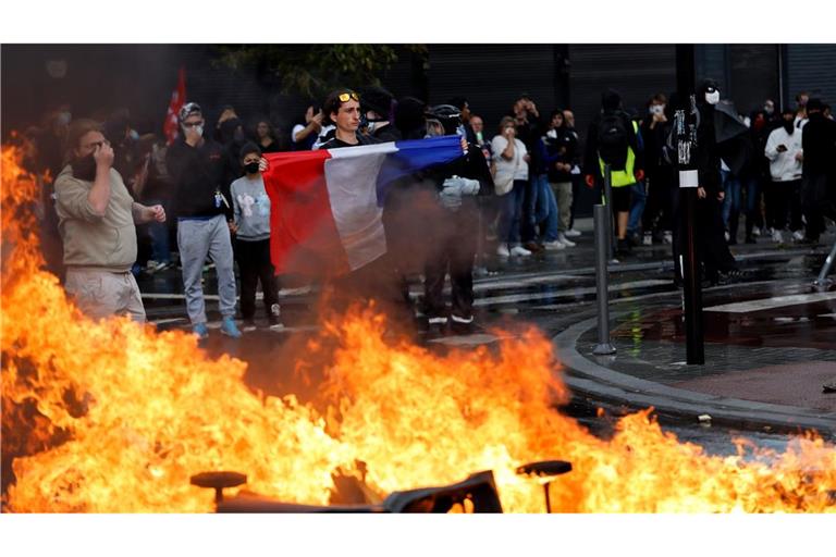 Ein Demonstrant der Protestbewegung "Bloquons Tout" (Alles blockieren) zeigt eine französische Nationalflagge neben brennenden Mülltonnen.