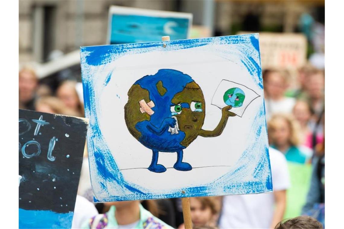 Ein Demonstrant geht mit einem Plakat mit einer gezeichneten weinenden Erde durch die Stadt. Foto: Christophe Gateau/Archivbild