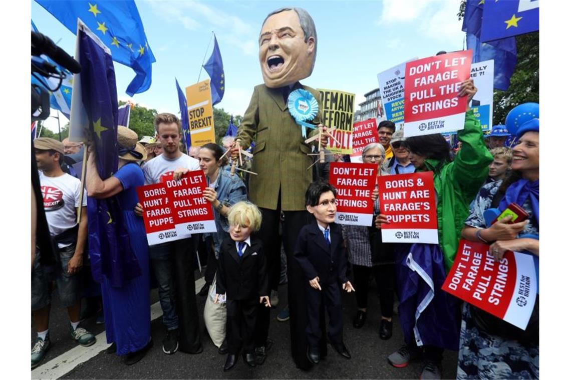 Anti-Brexit-Demo in London: Riesen-Puppe verspottet Johnson Ein Demonstrant (M) hat sich für den Protestzug als Nigel Farage, Vorsitzender der Brexit-Partei, verkleidet - und hält die Schnüre der Marionetten „Boris Johnson“ und „Jeremy Hunt“ in den Händen. Foto: Aaron Chown/PA Wire