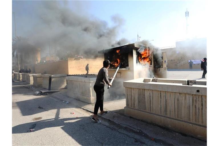 Ein Demonstrant schürt vor der Botschaft der Vereinigten Staaten ein Feuer. Mehrere Hundert Demonstranten haben die US-Botschaft in der Hauptstadt Bagdad attackiert und versucht, das Botschaftsgelände zu stürmen. Foto: Khalil Dawood/XinHua/dpa
