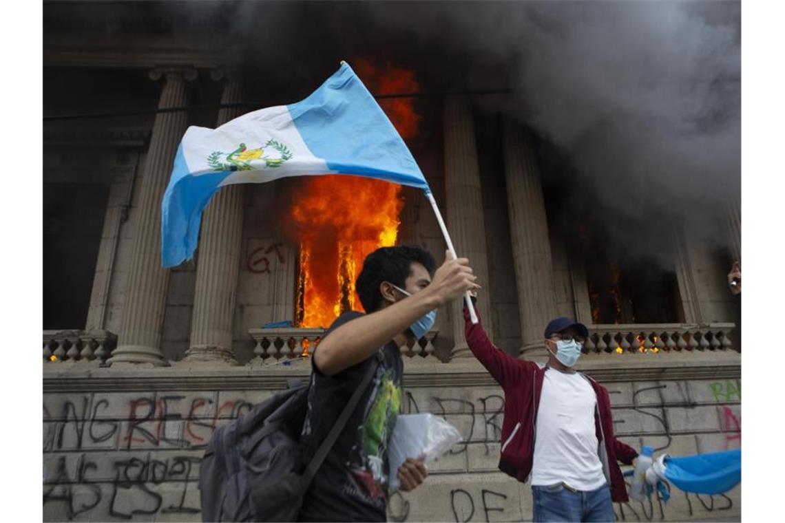 Protest gegen Haushalt: Kongress in Guatemala brennt Ein Demonstrant schwenkt vor dem brennenden Kongress die Nationalfahne. Foto: Oliver De Ros/AP/dpa