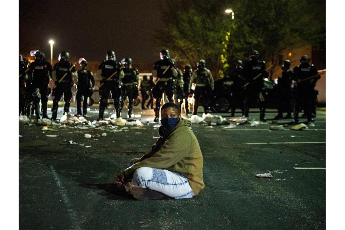 Ein Demonstrant sitzt in Minnesota als Protest auf einer Straße vor einer Reihe von Bereitschaftspolizisten. Foto: Imagespace/imageSPACE via ZUMA Wire/dpa