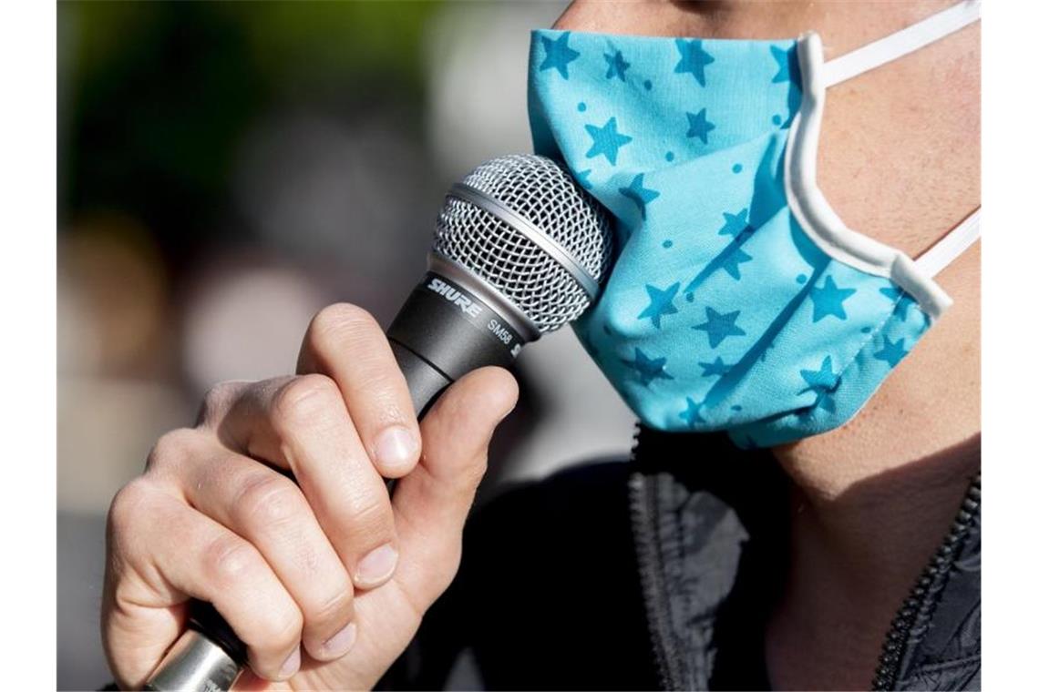 Ein Demonstrant spricht bei einer Kundgebung durch einen Mund-Nasen-Schutz in ein Mikrofon. Foto: Christoph Soeder/dpa