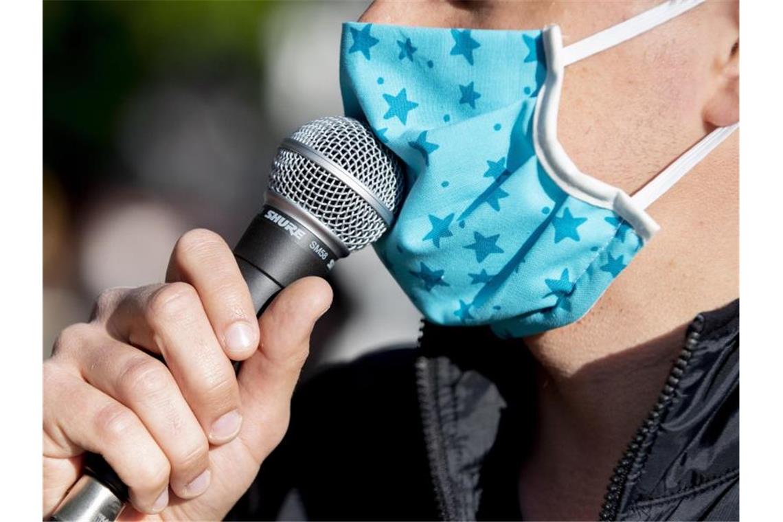 Ein Demonstrant spricht mit Mundschutz in ein Mikrofon. Foto: Christoph Soeder/dpa/Symbolbild