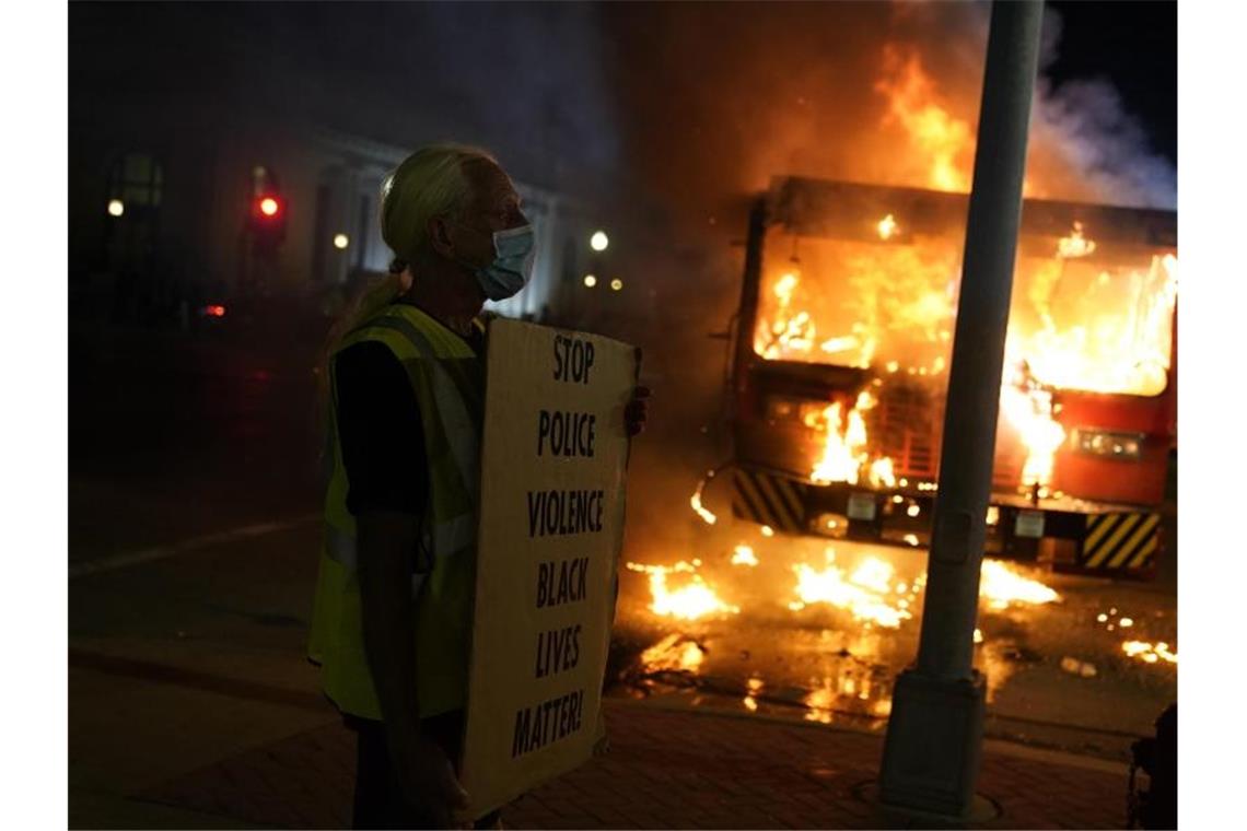 Ein Demonstrant steht mit einem Transparentvor einem brennenden Müllwagen. Foto: David Goldman/AP/dpa