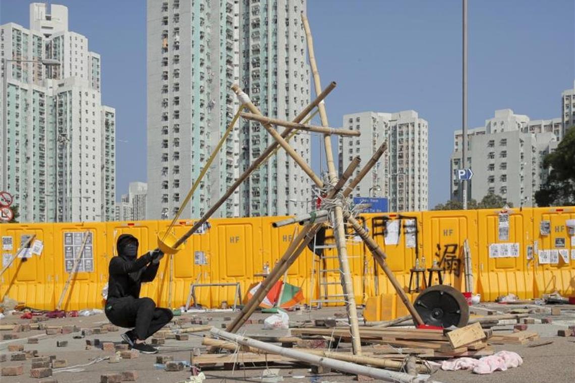 Ein Demonstrant testet eine selbstgebaute Schleuder, bei der ein gelber Helm zwischen Spanngummis sitzt, in der Nähe der Hong Kong Baptist University. Foto: Kin Cheung/AP/dpa