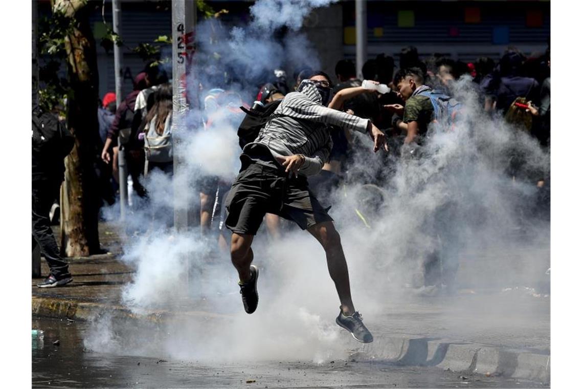 Ein Demonstrant wirft bei Protesten in Santiago de Chile eine Tränengasgranate zurück auf Polizisten. Foto: Miguel Arenas/AP/dpa