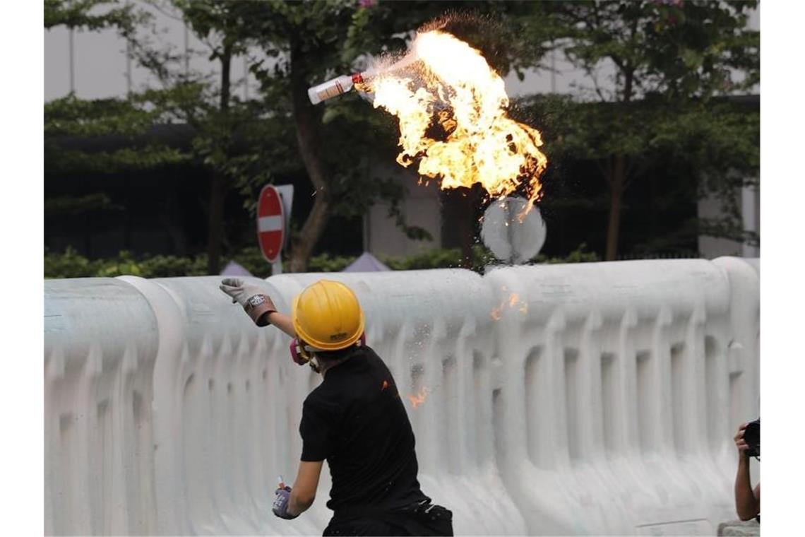 Ein Demonstrant wirft einen Molotowcocktail über eine Absperrung. Am Rande der Proteste kam es zu Zwischenfällen. Foto: Vincent Thian/AP