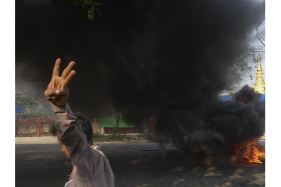 Myanmar: Inhaftierter dpa-Journalist frei - Neue Proteste Ein Demonstrant zeigt den Dreifingergruß als Zeichen des Widerstands, als er in Yangon an brennenden Reifen vorbeigeht. Foto: Uncredited/AP/dpa