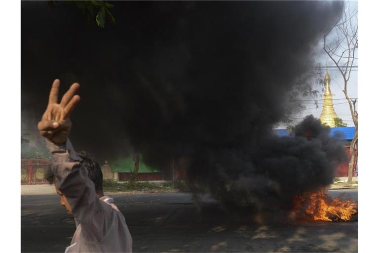 Ein Demonstrant zeigt den Dreifingergruß als Zeichen des Widerstands vor brennenden Reifen in Yangon. Foto: Uncredited/AP/dpa