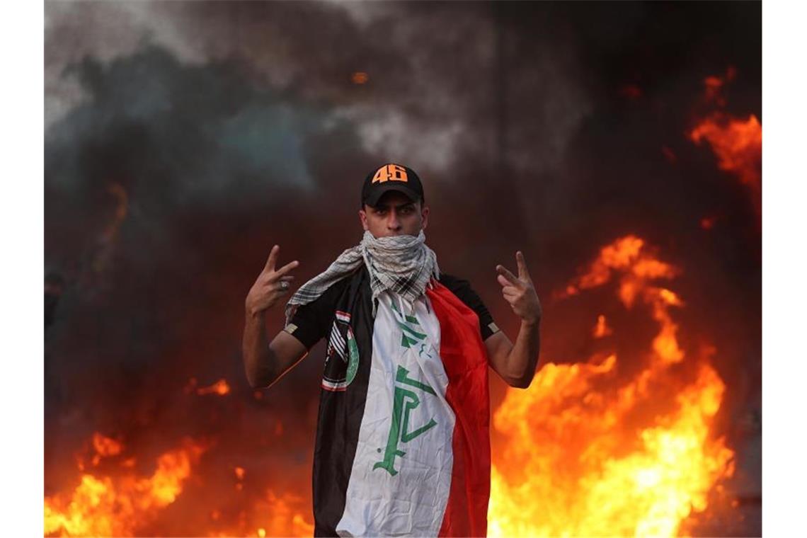 Mindestens 38 Tote bei Protesten im Irak Ein Demonstrant zeigt vor lodernden Flammen das Siegeszeichen. In mehreren Provinzen stürmten die Protestler Gebäude und legten Feuer. Viele Iraker klagen über die vernachlässigte Infrastruktur sowie über die Arbeitslosigkeit. Foto: Hadi Mizban/AP/dpa