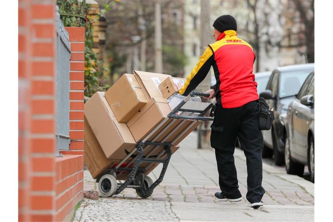 Ein DHL-Paketzusteller geht mit einer Sackkarre voller Pakete zu einem Haus. Foto: Jan Woitas/zb/dpa