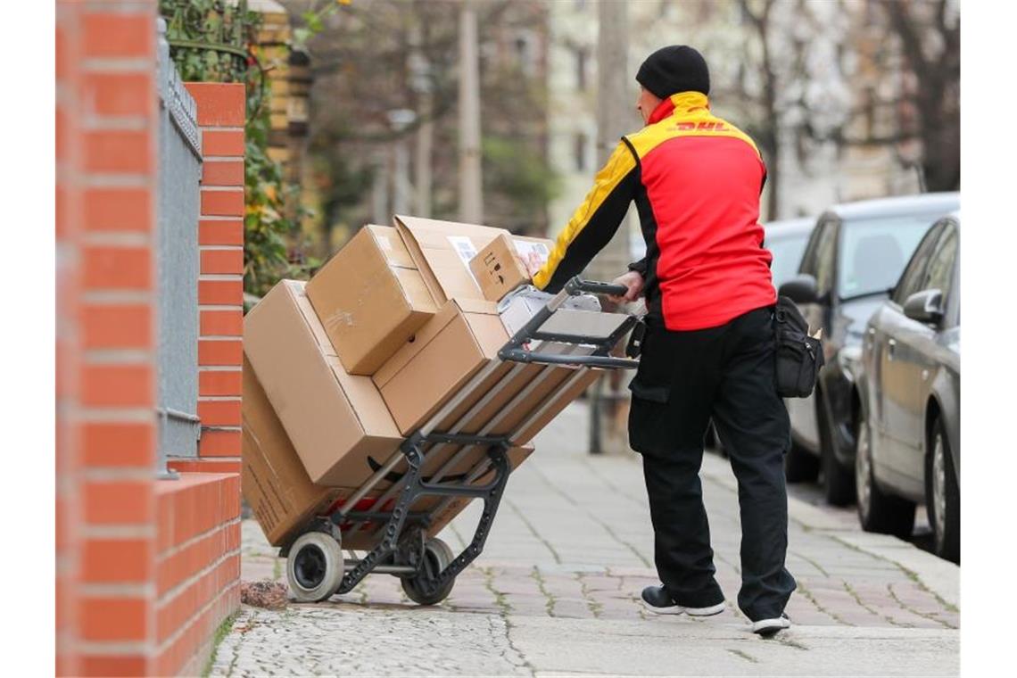 Ein DHL-Paketzusteller geht mit einer Sackkarre voller Pakete zu einem Haus. Foto: Jan Woitas/zb/dpa