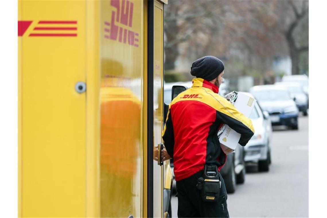 Ein DHL-Paketzusteller verlässt mit mehreren Sendungen sein Fahrzeug. Foto: Jan Woitas/zb/dpa