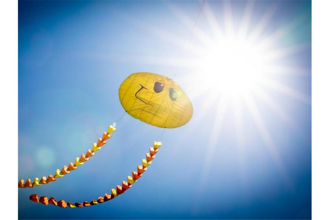 Ein Drache in Form eines Smileys fliegt am blauen Himmel vor der Sonne. Foto: Moritz Frankenberg/dpa/Archivbild