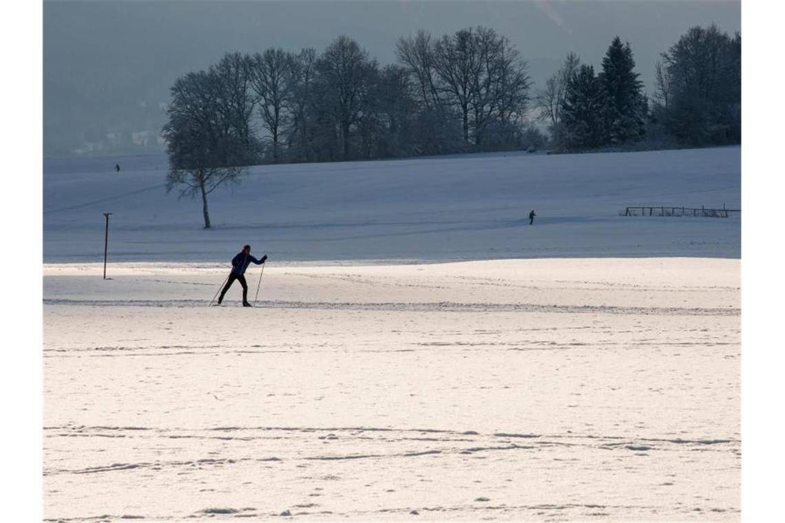 Ein einsamer Langläufer zieht im bayerischen Ettal seine Spur durch die verschneite Gegend. Foto: Peter Kneffel/dpa