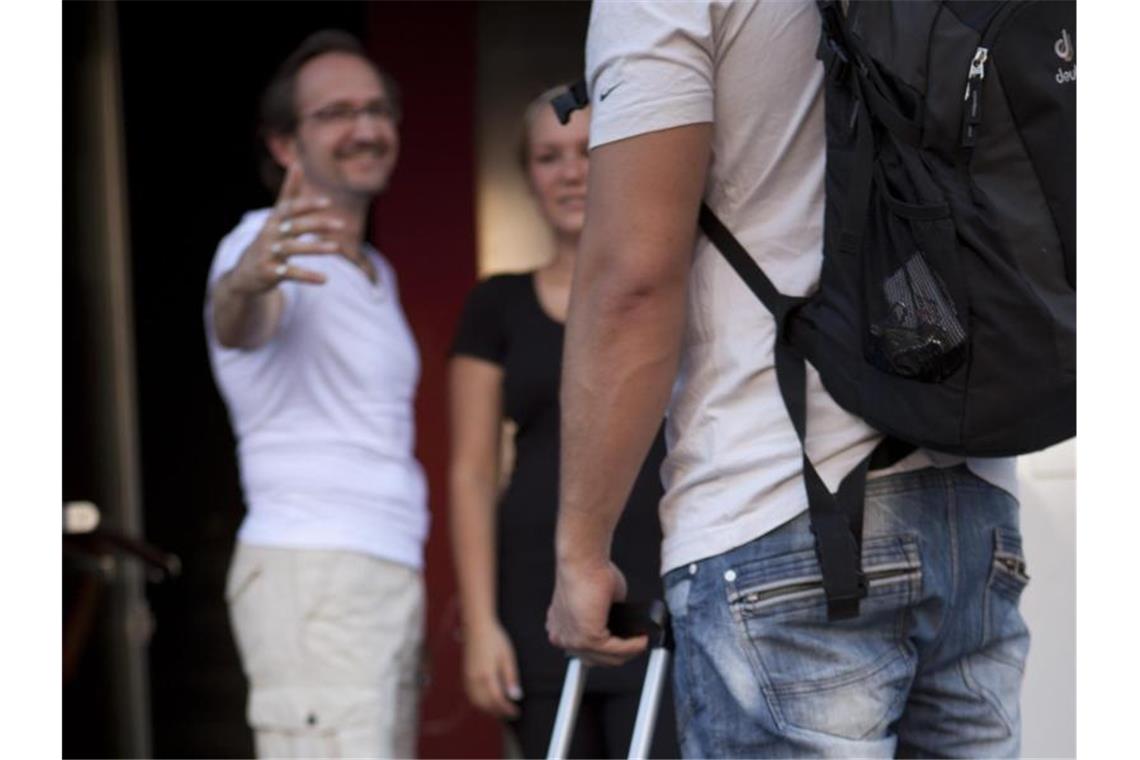 Kinder machen glücklich: Wenn sie aus dem Haus sind Ein Erwachsener (r) steht mit einem Rollkoffer in der Hand vor einem älteren Paar. Foto: Silvia Marks/Archivbild